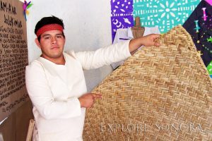 A man dressed in traditional Tohono O'odham clothing holds a petate